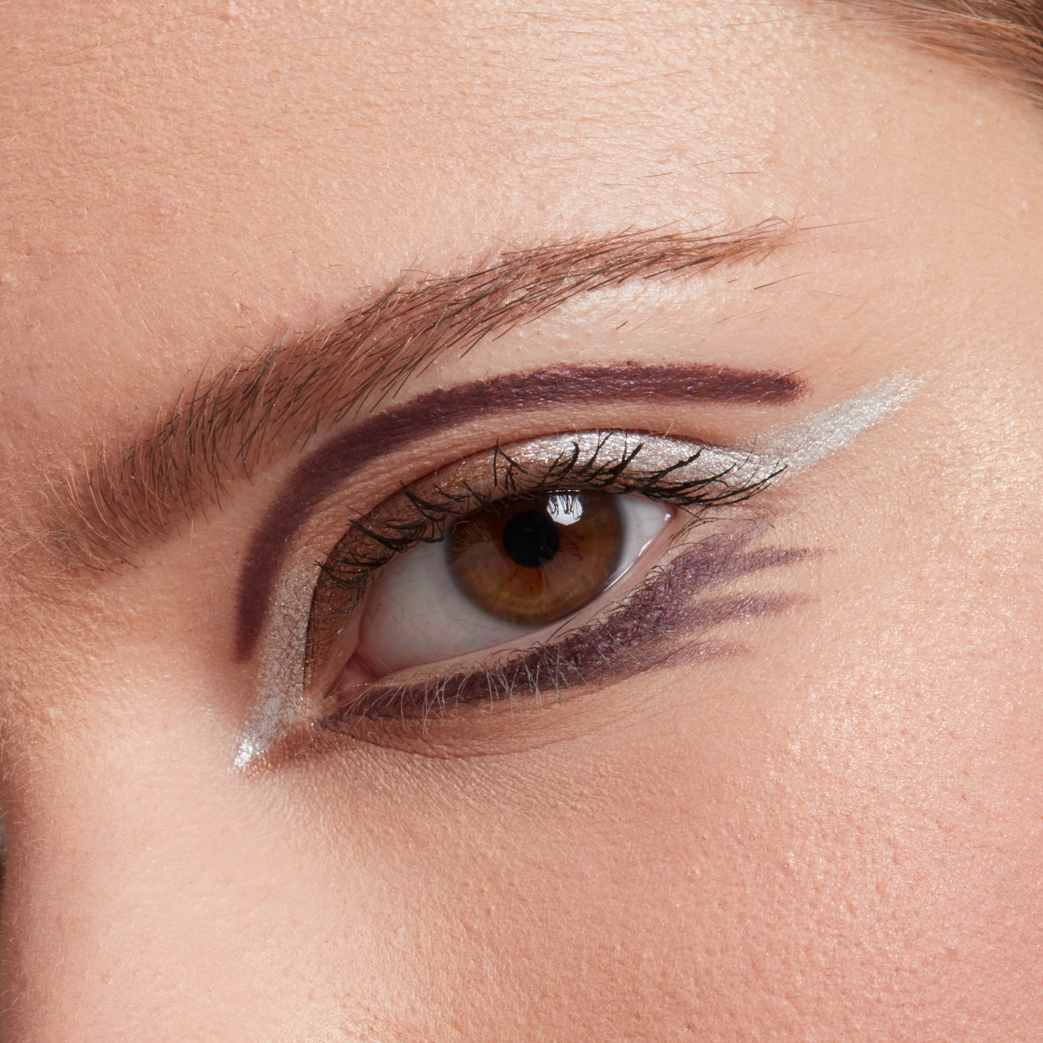 A close up image of a models eye with brown, purple, and white touches of NYX Cosmetics eyeliner. 