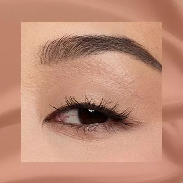 Close-up of an eye area with NYX Professional Makeup Lid Lingerie Cream Eye Pigment in 03 Beige Appeal, shown on a tan matte textured background.