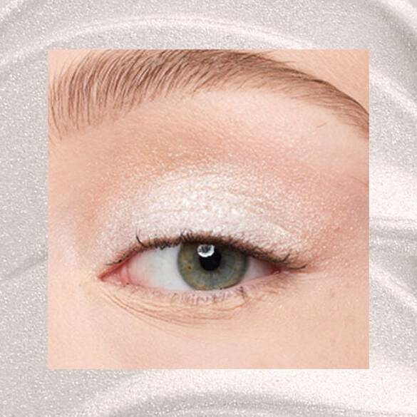 Close-up of an eye area with NYX Professional Makeup Lid Lingerie Cream Eye Pigment in 01 Satin Silver, shown on a shimmering silver textured background.