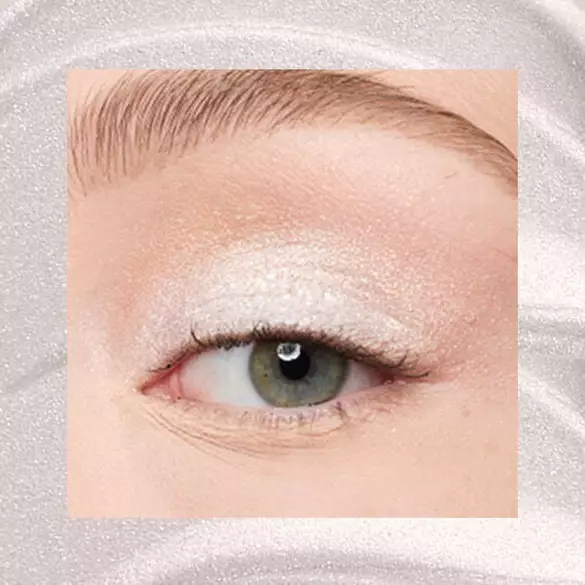 Close-up of an eye area with NYX Professional Makeup Lid Lingerie Cream Eye Pigment in 01 Satin Silver, shown on a shimmering silver textured background.