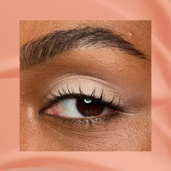 Close-up of an eye area with NYX Professional Makeup Lid Lingerie Cream Eye Pigment in 02 In-Nude-Endo, shown on a nude matte textured background.
